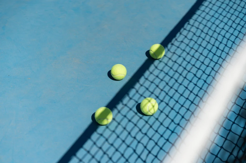 Three tennis balls scattered on a blue court with a shadowed net.