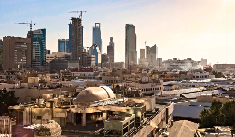 Skyline of Riyadh, Saudi Arabia featuring modern skyscrapers and construction cranes at sunset.