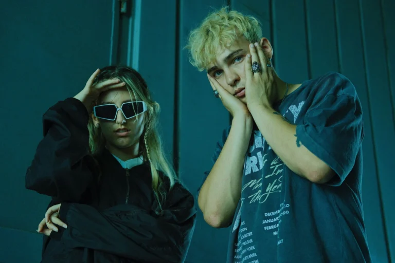 Trendy man and woman pose in urban environment wearing stylish outfits and accessories.