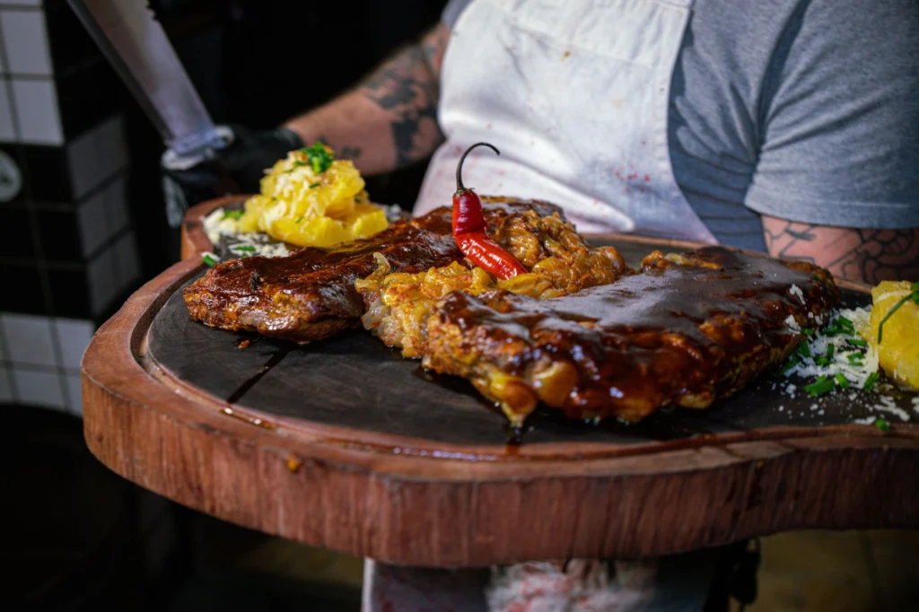 Barbecued ribs with spicy sauce and garnish served on a rustic wooden platter.