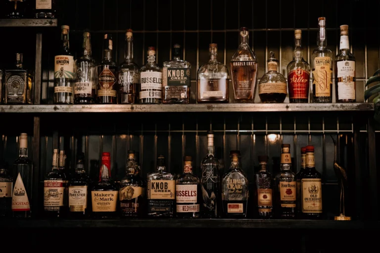 A variety of liquor bottles arranged on shelves in a dimly lit bar setting.