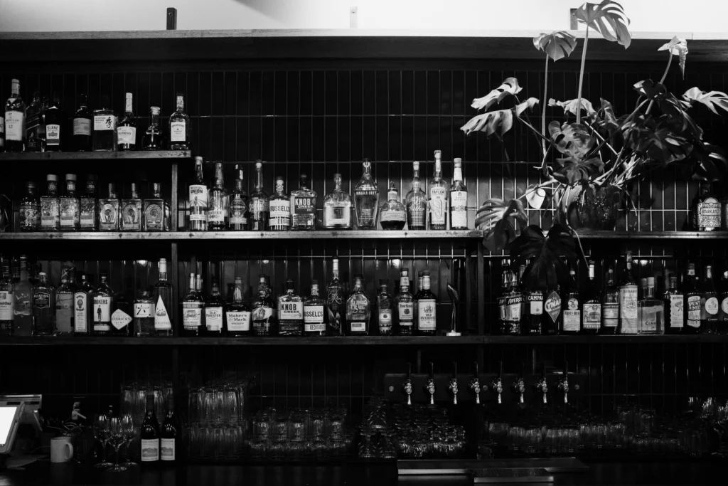 A black and white image showcasing liquor bottles on bar shelves with plants.