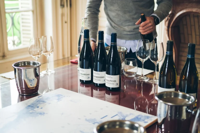 A sommelier pouring wine from bottles on a restaurant table with glasses and buckets.