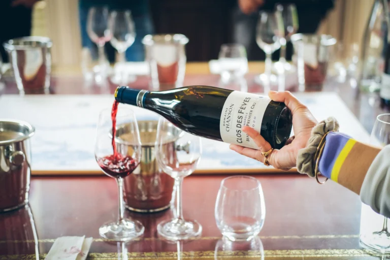 A hand gracefully pours red wine into a glass on a dining table, creating an elegant atmosphere.