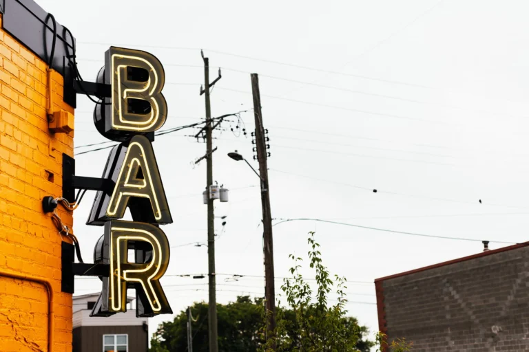 A neon bar sign on a yellow brick wall with urban power lines in Chattanooga.