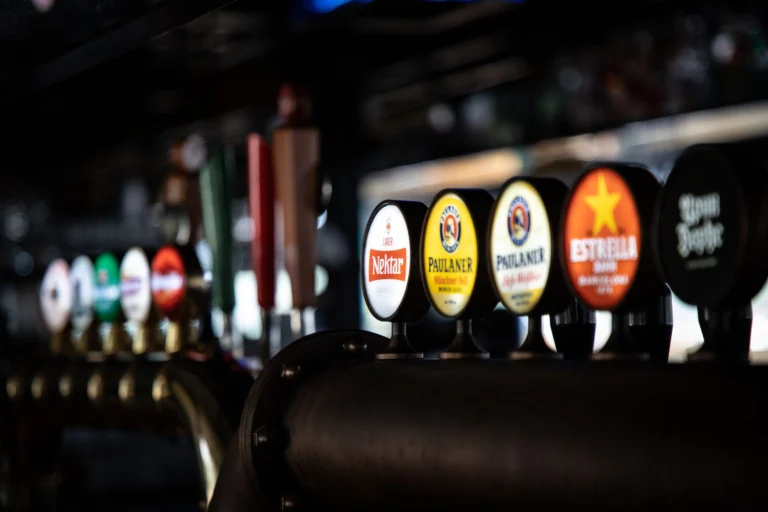Close-up of assorted beer taps in a dimly lit bar, showcasing various brewery logos and selections.