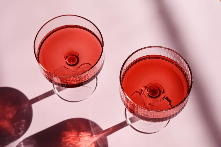 Two elegant red cocktails elegantly served in crystal glasses casting artistic shadows.