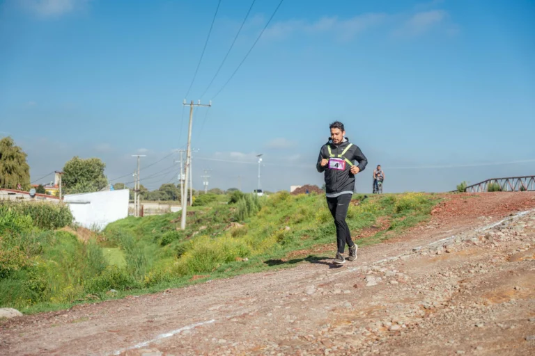 Athlete running on a dirt path in an outdoor race, wearing sportswear and a race bib.