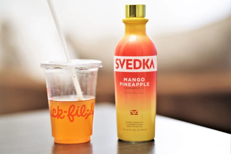 A vibrant mango pineapple vodka bottle beside a branded drink cup, perfectly captured.