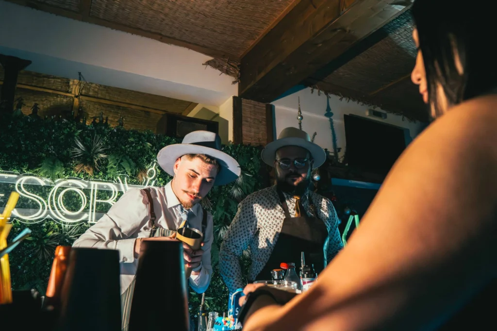 Bartenders crafting cocktails in a lively bar with neon lights and a vibrant atmosphere.