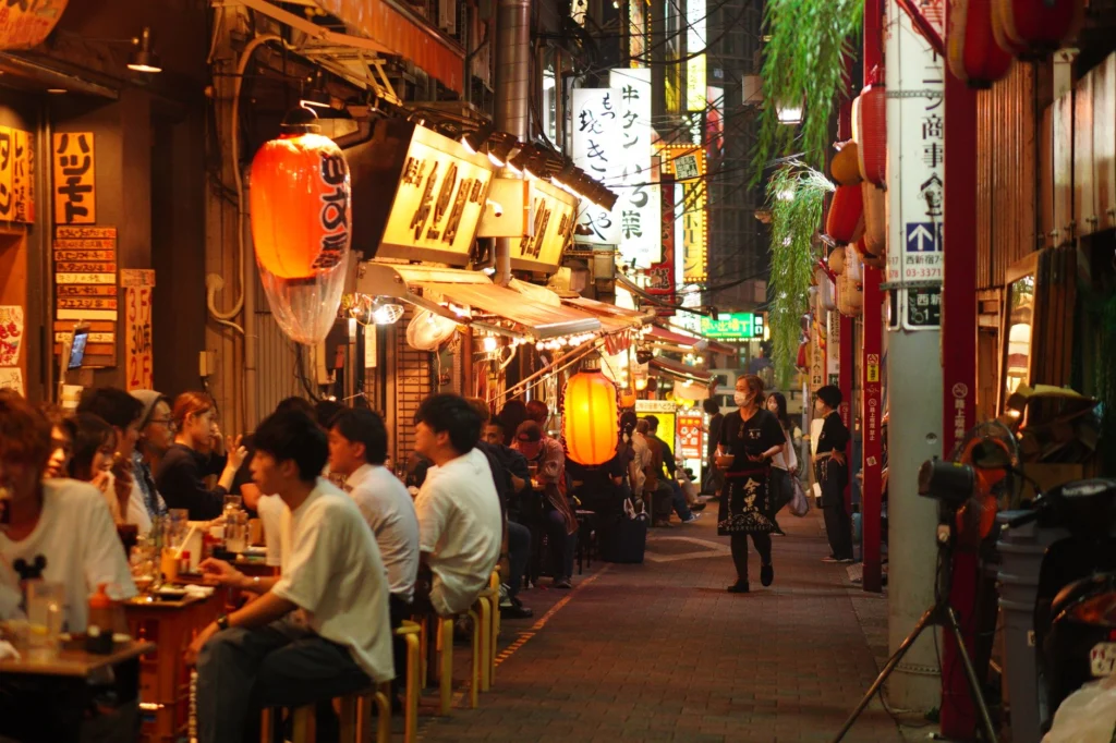 Night scene of people dining in a lively alley in Shinjuku City, Tokyo, illuminated by paper lanterns.