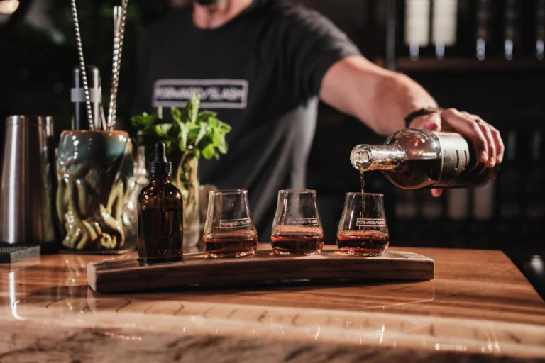 Bartender pouring whiskey into glasses at a bar with cocktail setups in view.