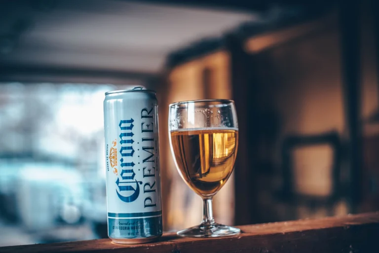 Close-up of a glass of beer and an aluminum can indoors with warm lighting.
