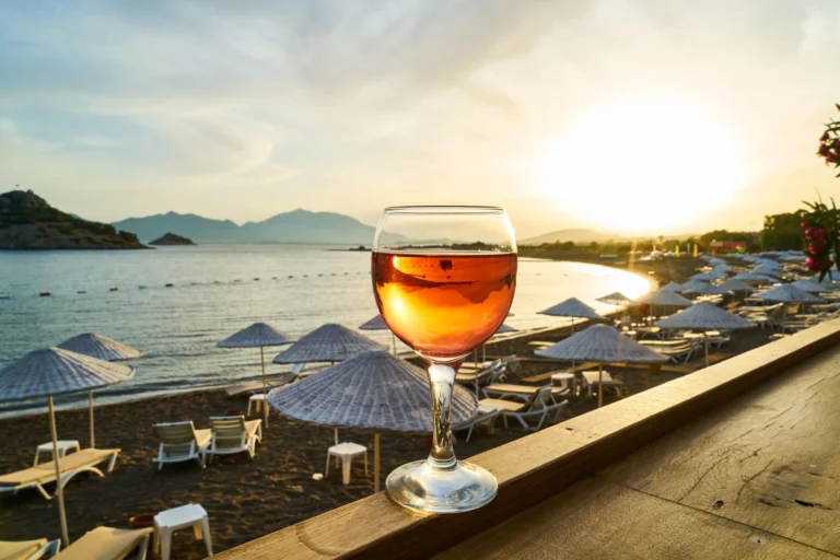 Scenic sunset over the beach with a cocktail glass in the foreground, capturing the perfect holiday vibe.