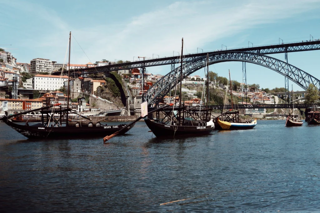 Discover the iconic Luís I Bridge in Porto with traditional sailboats on the Douro River.