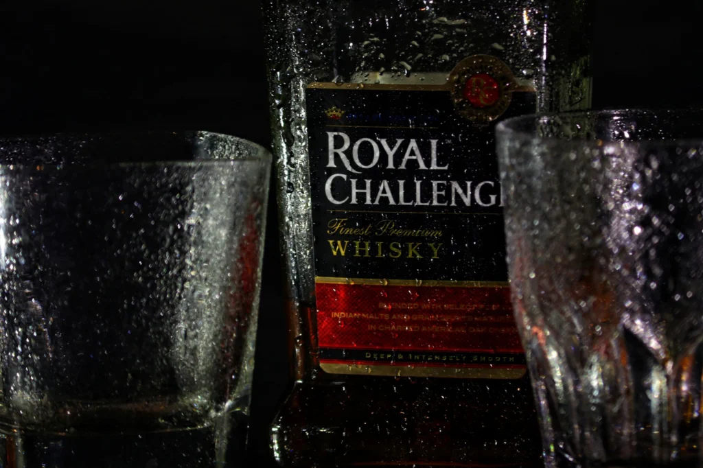 Close-up shot of Royal Challenge whiskey bottle with glasses.