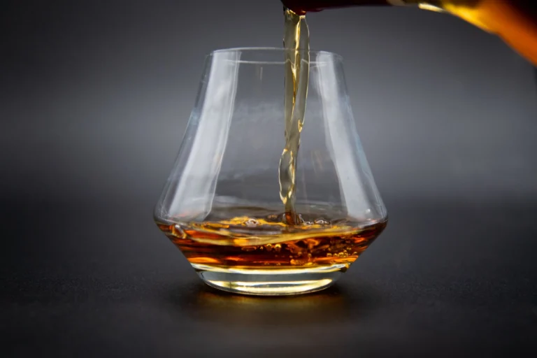 Aesthetic shot of whiskey being poured into a glass against a dark background.