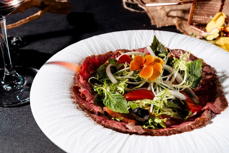 A fresh and vibrant gourmet beef carpaccio dish with leafy greens and edible flower garnish.