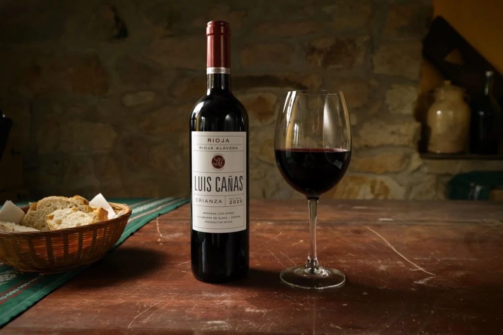 Luis Cañas wine bottle with a glass on a vintage wooden table, perfect for dining settings.