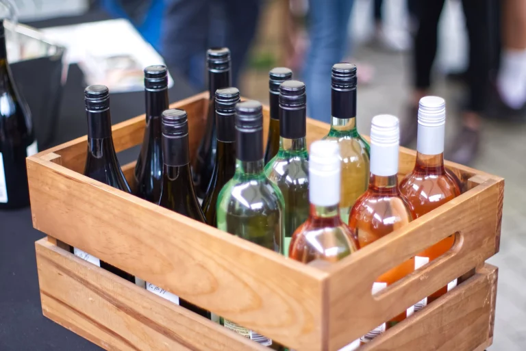 A wooden crate filled with diverse wine bottles at an outdoor gathering.