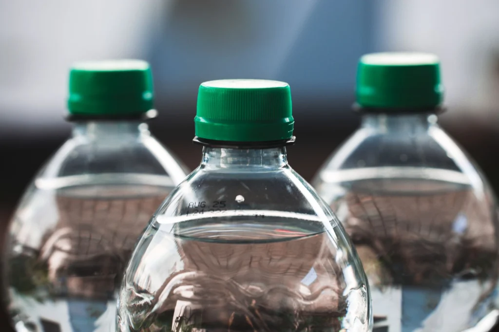 Focused view of three clear plastic bottles with green caps outdoors.