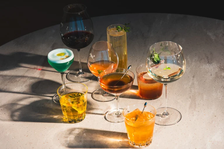 Vibrant cocktails in various glasses on a bar table, showcasing diverse colors and garnishes.