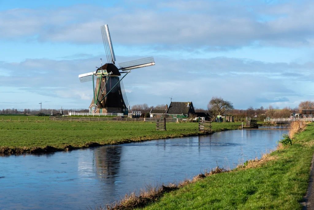 A scenic view of a traditional Dutch windmill beside a serene canal in the countryside.