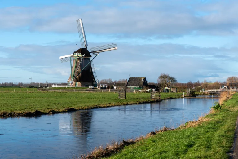 A scenic view of a traditional Dutch windmill beside a serene canal in the countryside.