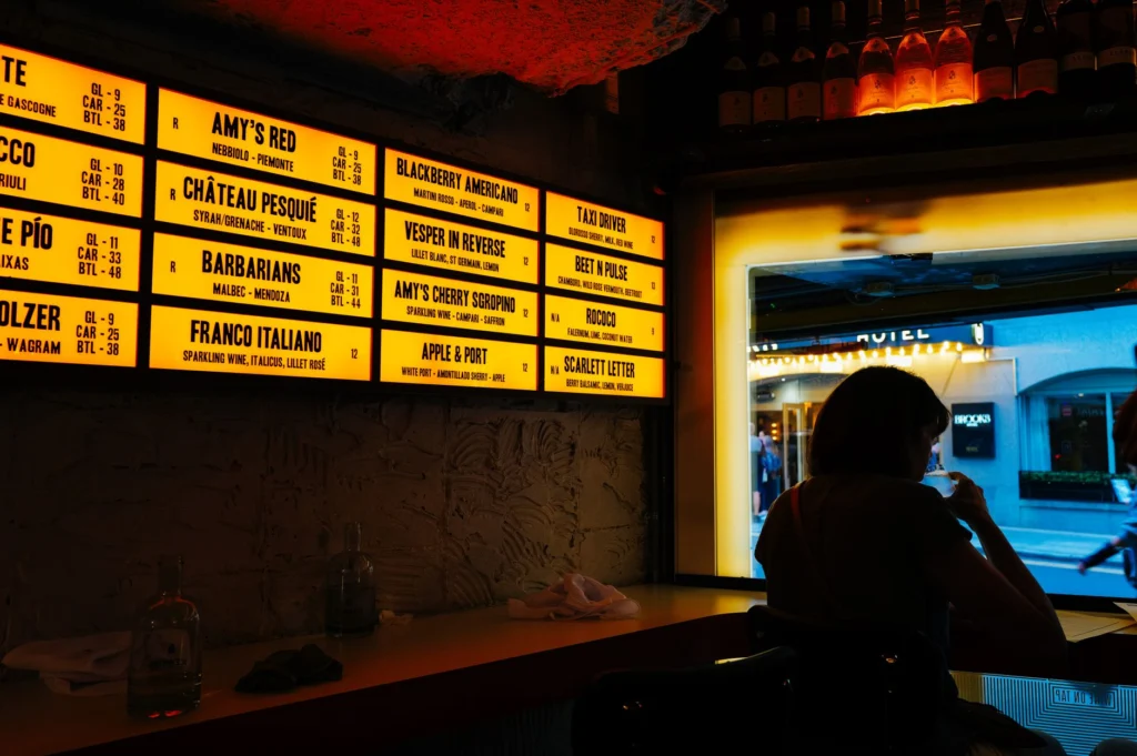 A dimly lit wine bar featuring a backlit menu board, creating a cozy ambiance.