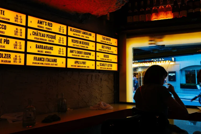 A dimly lit wine bar featuring a backlit menu board, creating a cozy ambiance.