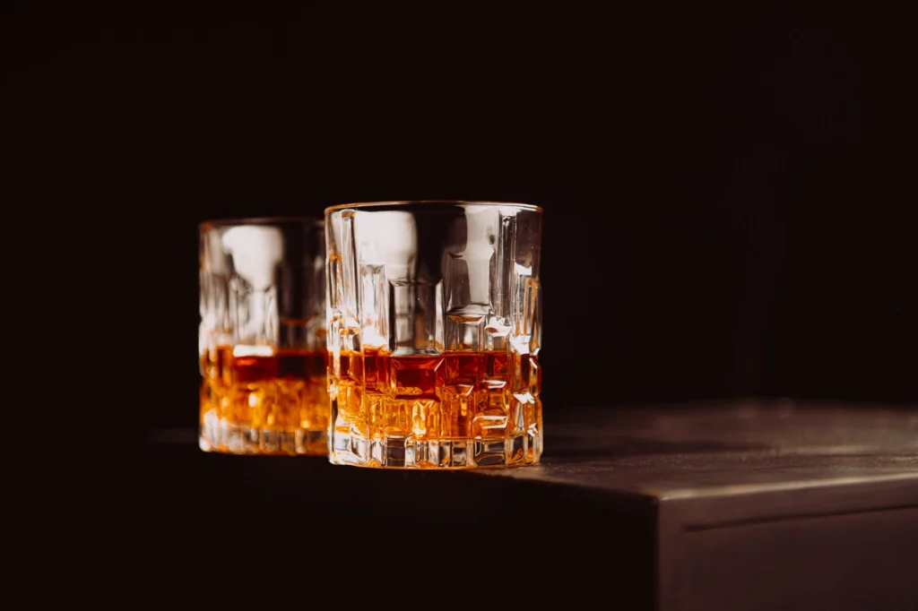 Two whiskey glasses with amber liquid on a dark surface, creating a cozy atmosphere.