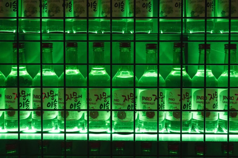 Illuminated bottles of Jinro Grapefruit soju on a vibrant green-lit shelf, creating a bold and artistic display.