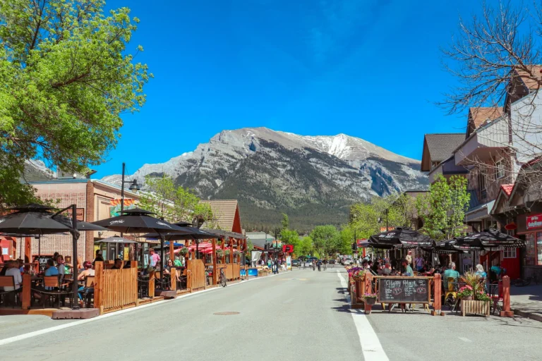 Lively street in Banff, Alberta with outdoor cafes and stunning mountain views, perfect for travel enthusiasts.