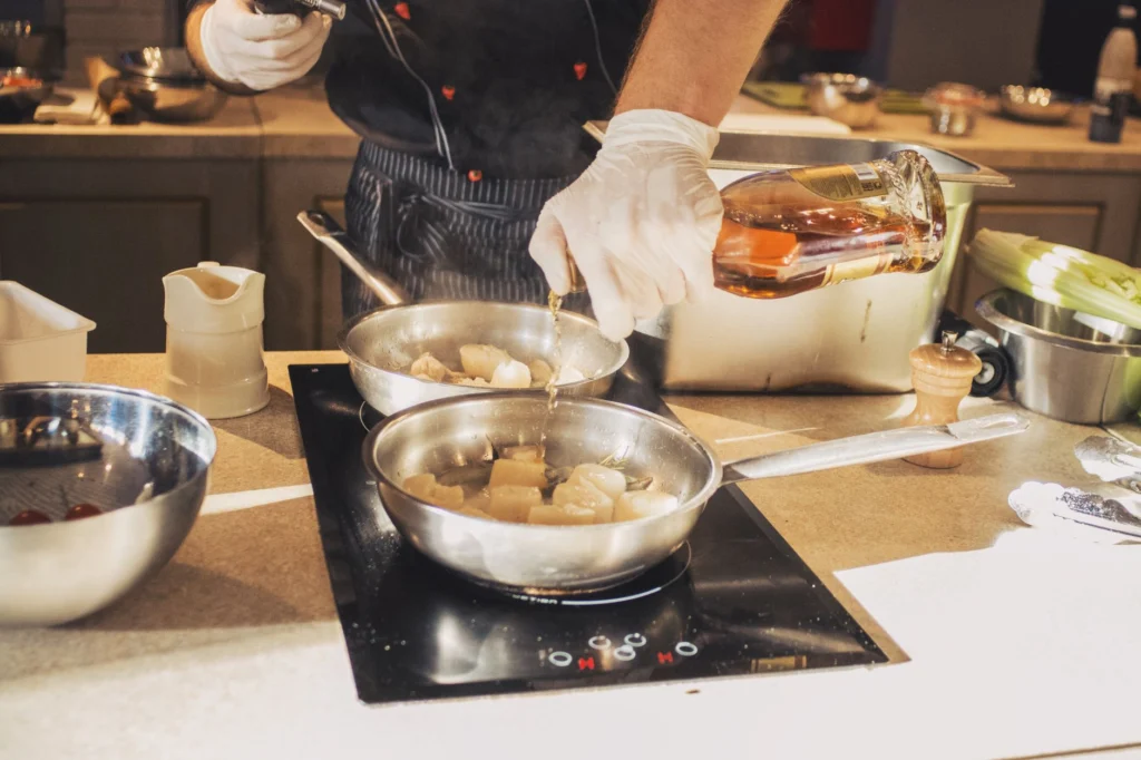 A chef adds whiskey to sautéing scallops in a professional kitchen setting.