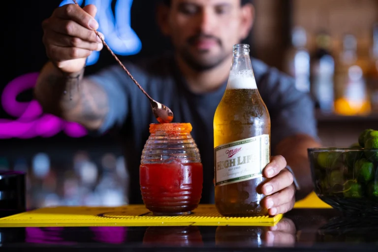 A bartender expertly prepares a michelada using Miller High Life beer in a vibrant bar setting.
