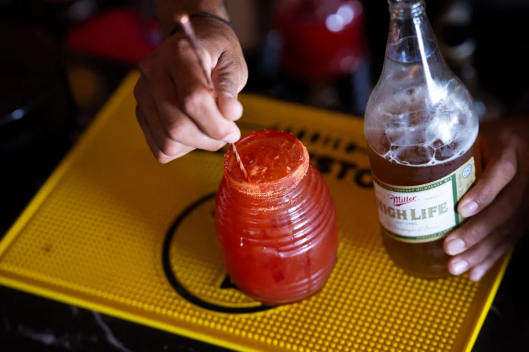 Close-up of crafting a michelada with spicy rim and beer at a bar, highlighting drink preparation.