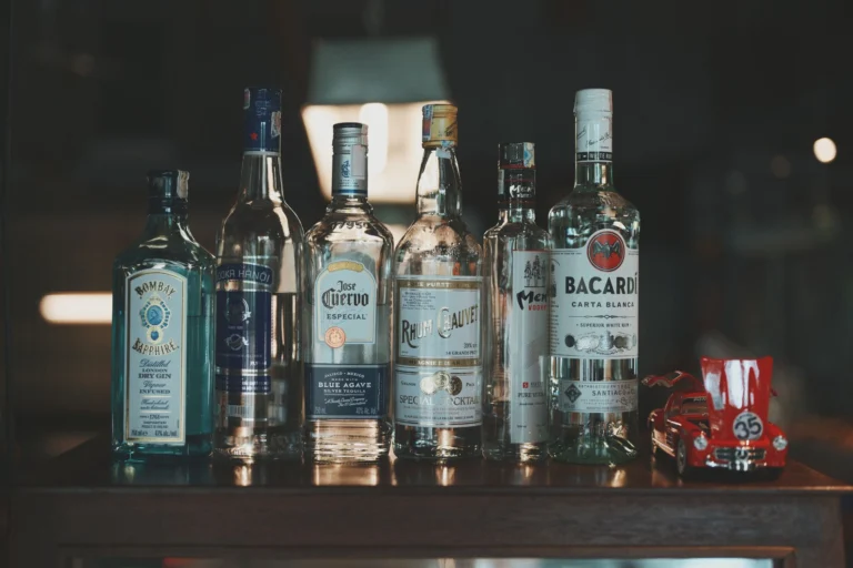Assorted alcohol bottles including gin, vodka, tequila, and rum displayed with a toy car for a stylish bar scene.