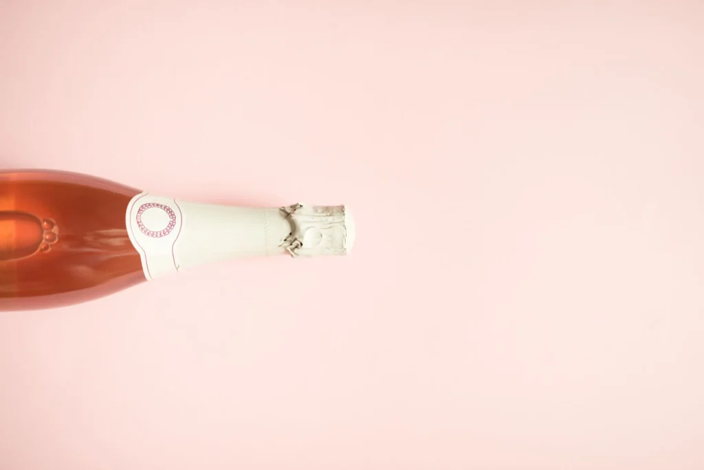 A minimalist champagne bottle laid on a pink backdrop, ideal for celebration themes.