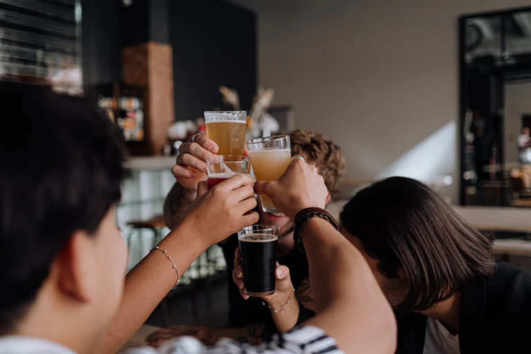 Friends raise glasses in a celebratory toast at a bar setting. Indoor lighting and social atmosphere.
