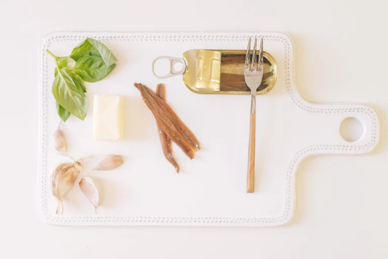 Flat lay photo of garlic, butter, herbs, and anchovies on a cutting board with a fork.