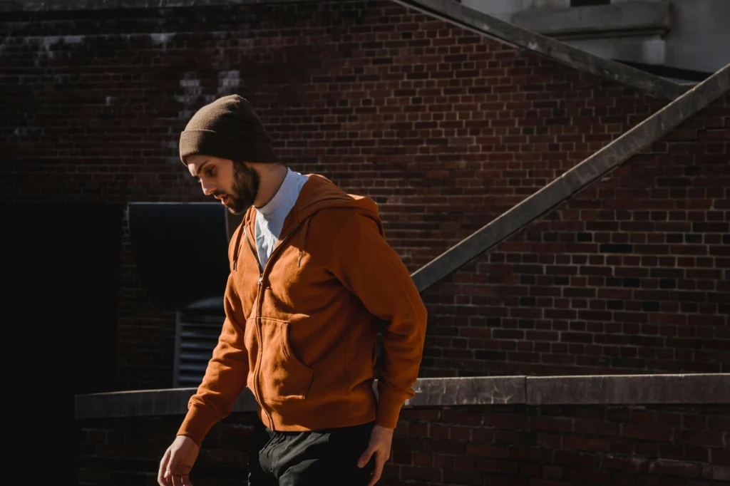 Young guy in warm outfit walking near brick wall with staircase in sunny day