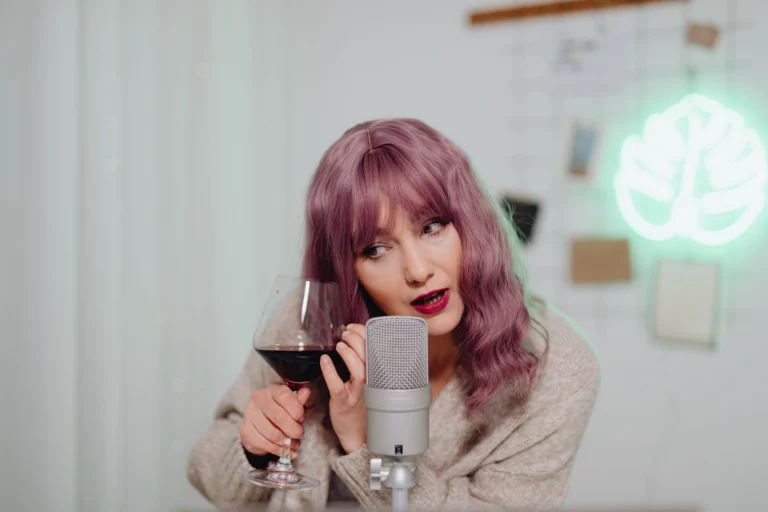 Woman with purple hair holding a wine glass, engaging in ASMR with a microphone.