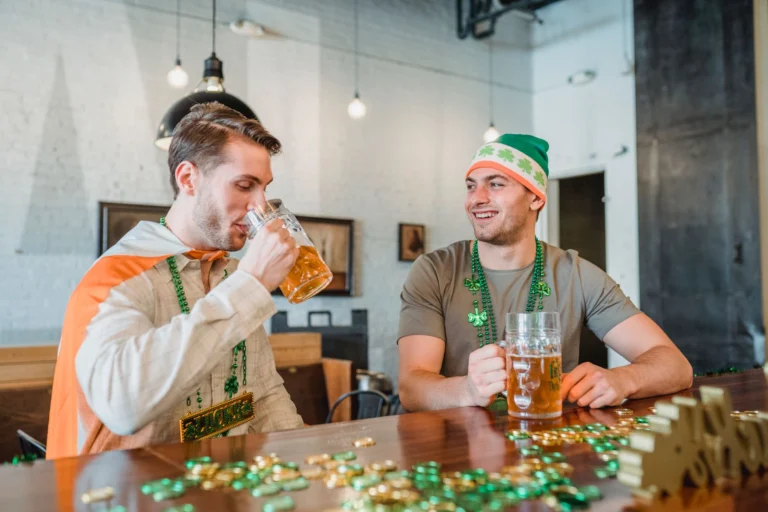 Two men enjoying beers indoors on St. Patrick's Day with festive decorations.