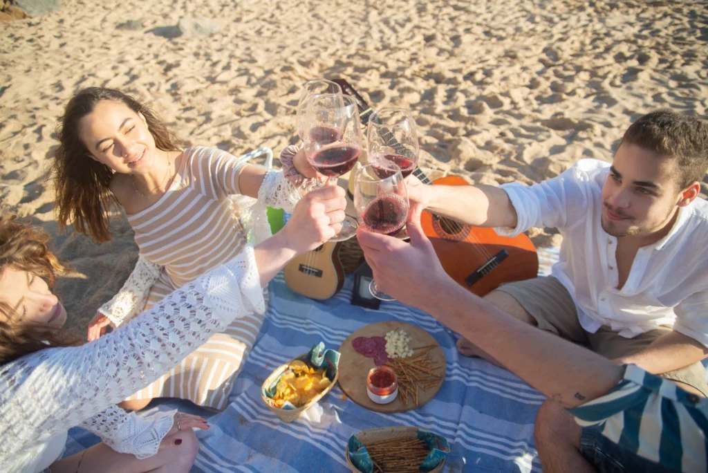 Group of friends enjoying a beach picnic in Portugal, toasting with wine glasses, creating joyful memories.