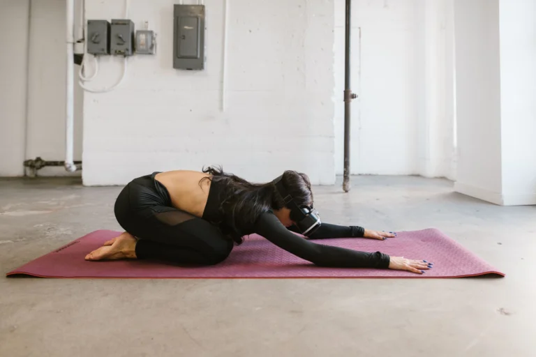 Adult woman using VR headset while performing yoga on a mat in a minimalist indoor setting.