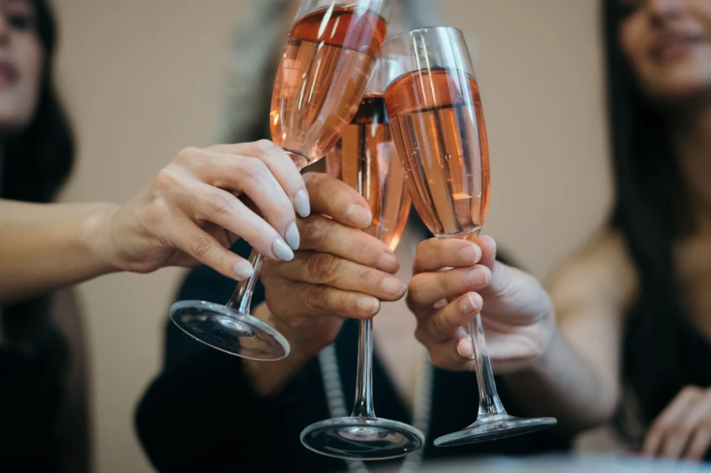 Close-up of four hands toasting with rosé wine glasses in a festive indoor setting.