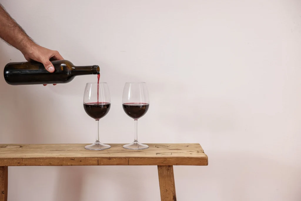 A person pours red wine into glasses on a rustic wooden table, elegant and simple.