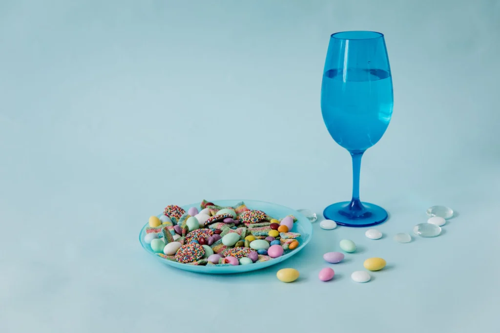 Colorful candies and a blue glass on pastel background, shot in studio.