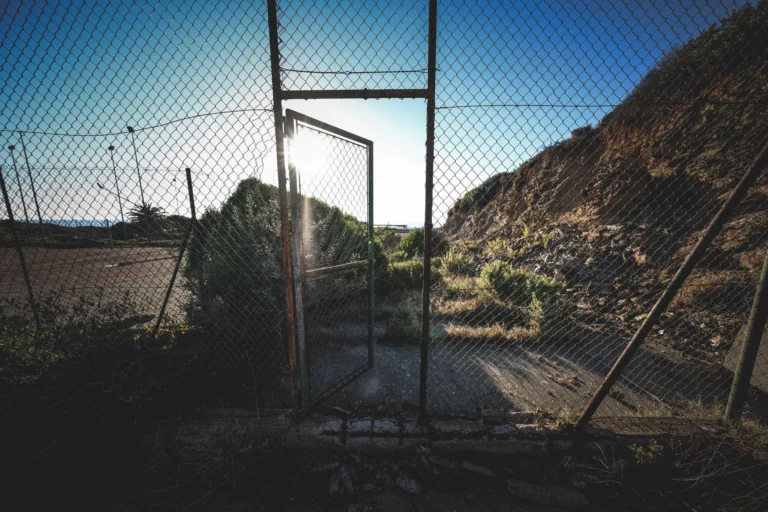 A rustic open fence gate leading to a grassy area with sunlight streaming through